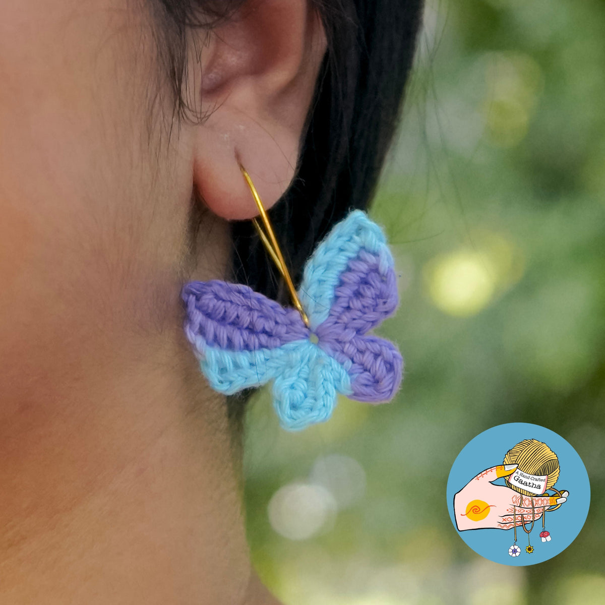 Model wearing handmade pastel blue and purple crochet butterfly hoop earrings outdoors.
