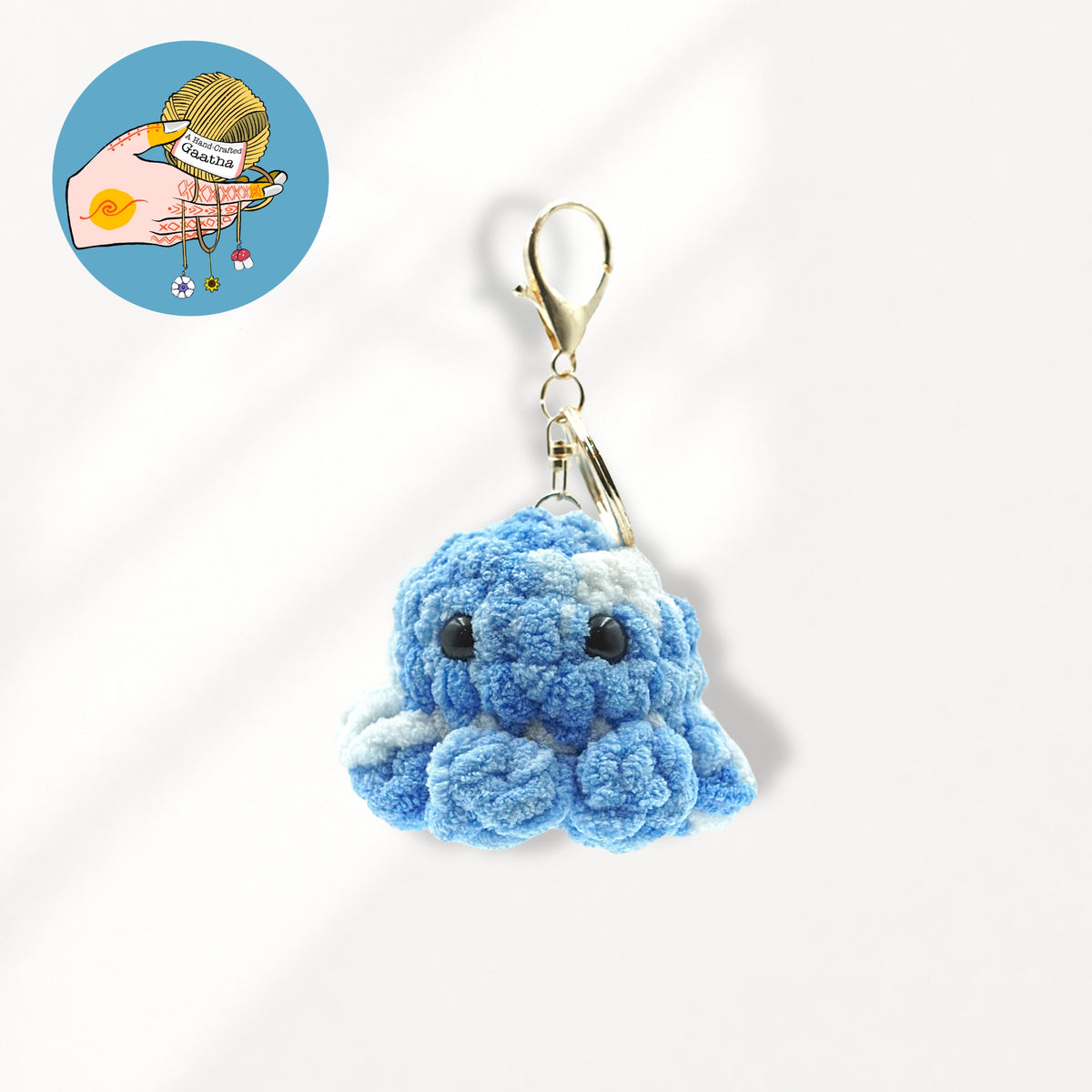 A blue and white crocheted octopus keychain charm with a gold lobster clasp.