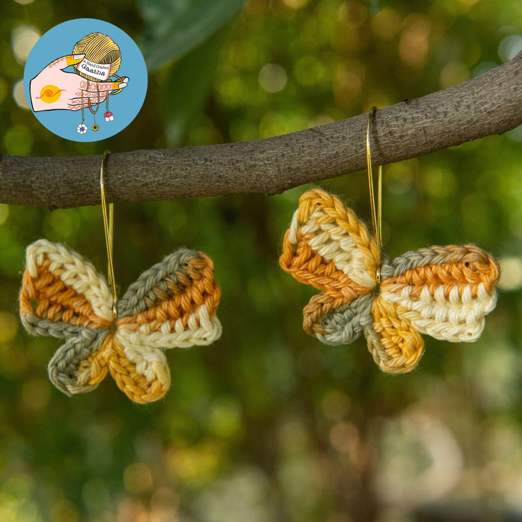 Earth toned crochet butterfly earrings hanging on tree branch outdoors.
