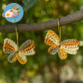 Earth toned crochet butterfly earrings hanging on tree branch outdoors.
