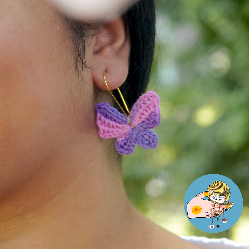 Close-up of a person wearing pink and purple butterfly earrings with a blurred green background.
