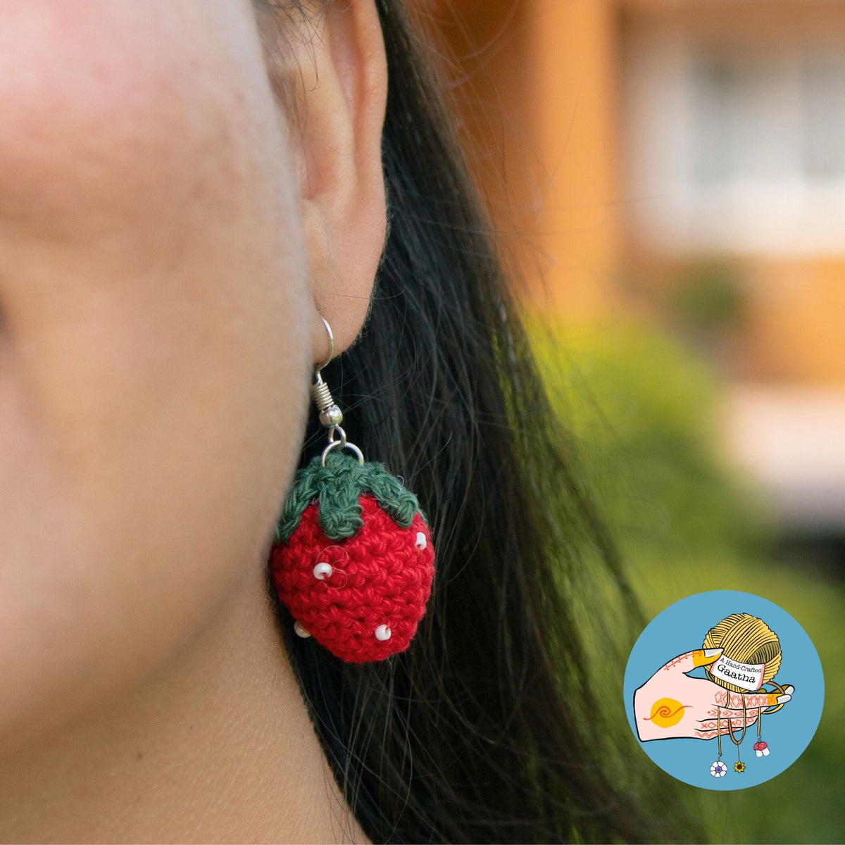 Close-up shot of a person wearing a vibrant red crochet strawberry earring with white bead accents and a green leafy top