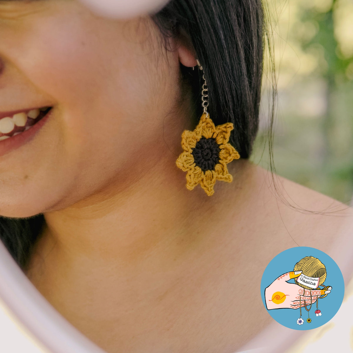 A smiling model wearing a large handcrafted crochet sunflower earring, showcasing the dangling boho jewelry design and its scale when worn.
