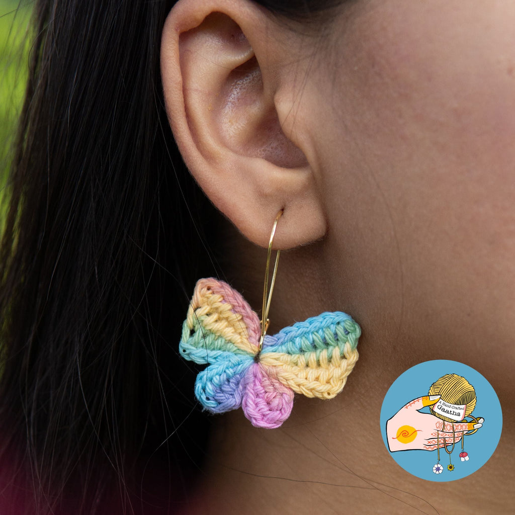 Model wearing handmade pastel rainbow crochet butterfly hoop earrings.