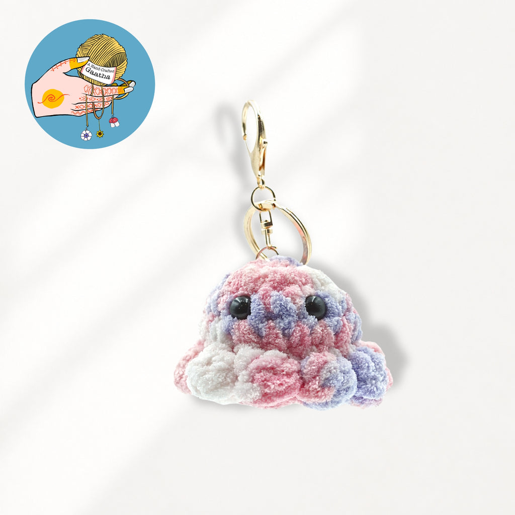 A crocheted octopus keychain charm in pink and white yarn, attached to a gold metal clasp and key ring.