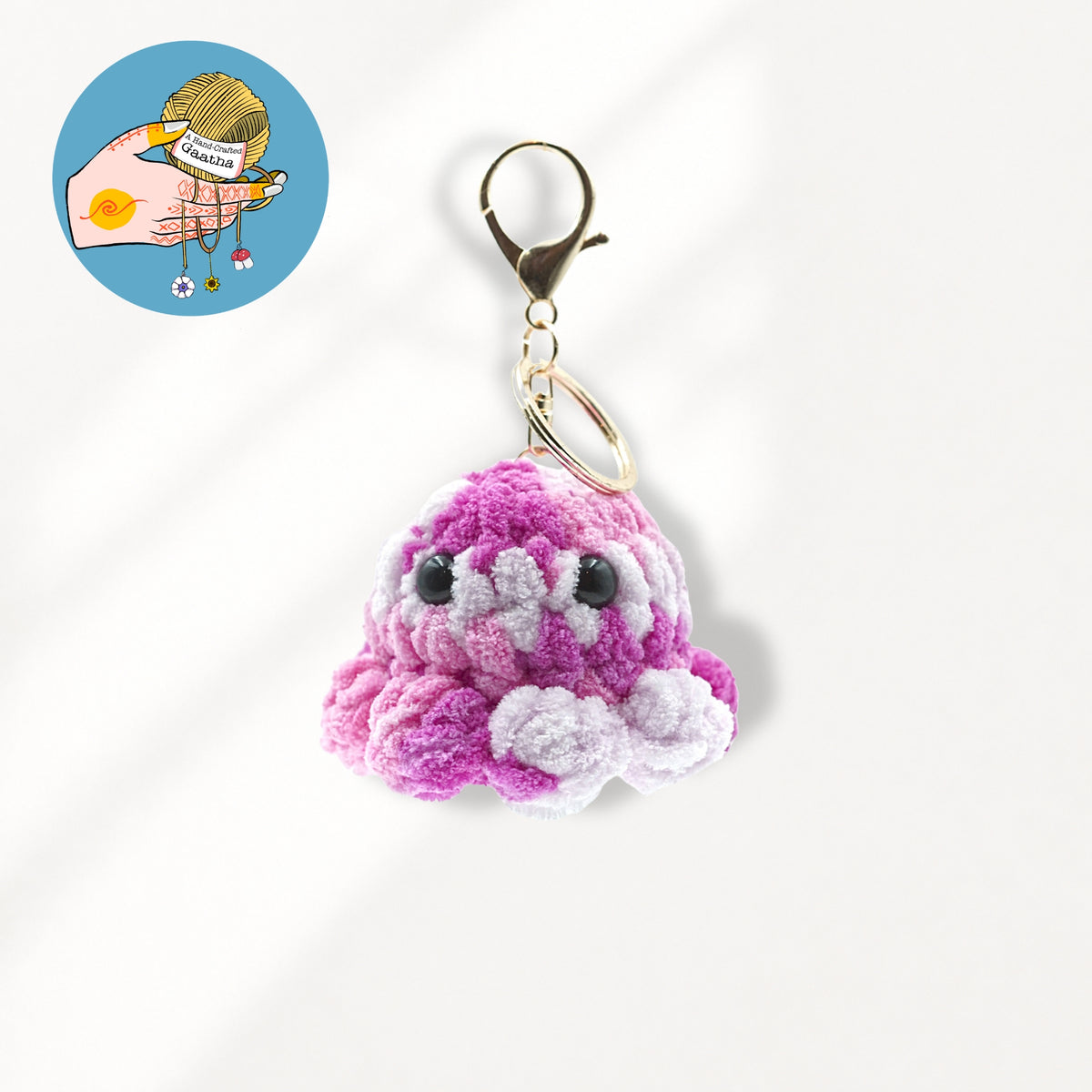 A small crocheted octopus keychain charm in pink with white accents, attached to a gold clasp.