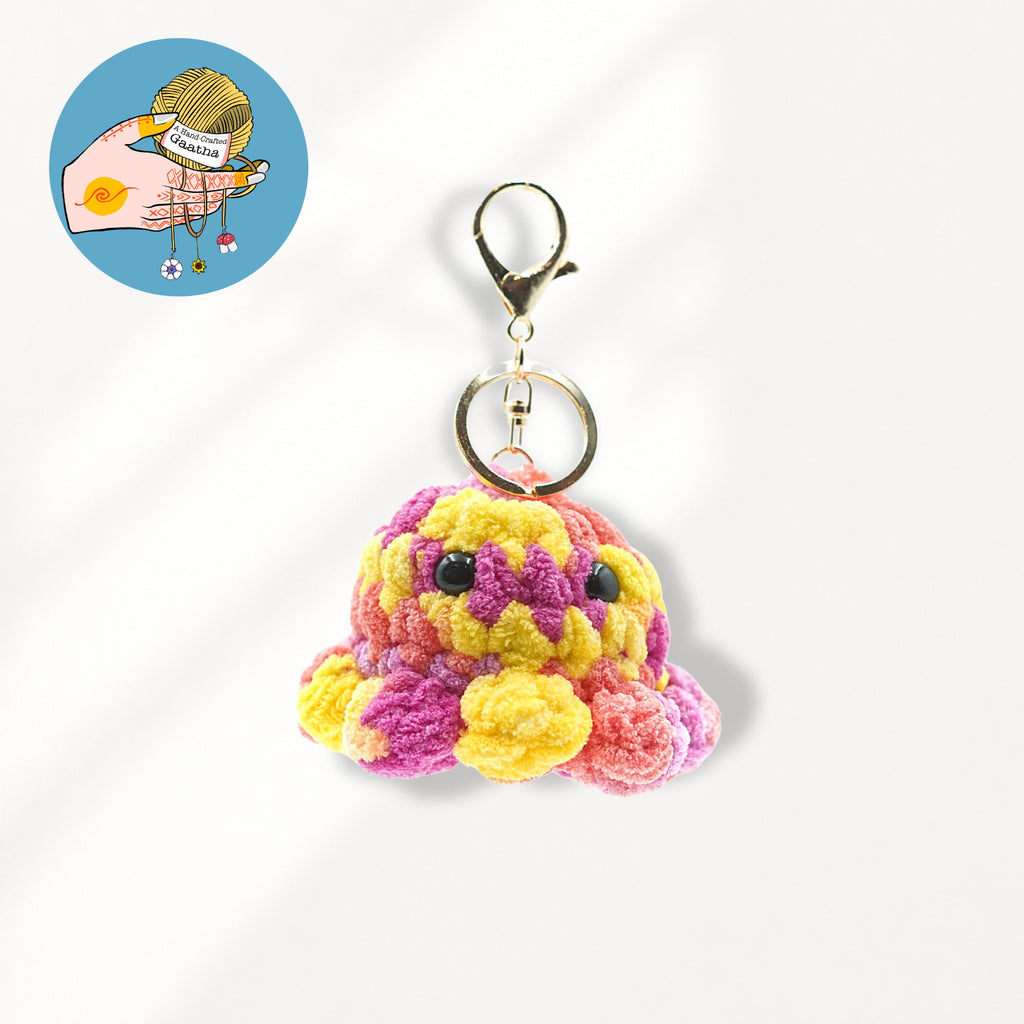A colorful crocheted octopus keychain charm with yellow, pink, and purple yarn, attached to a gold-tone lobster clasp and split ring.