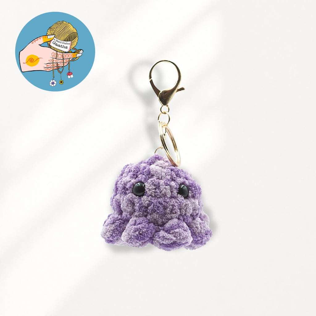 A small purple crocheted octopus keychain charm with black bead eyes and a gold-tone lobster clasp.