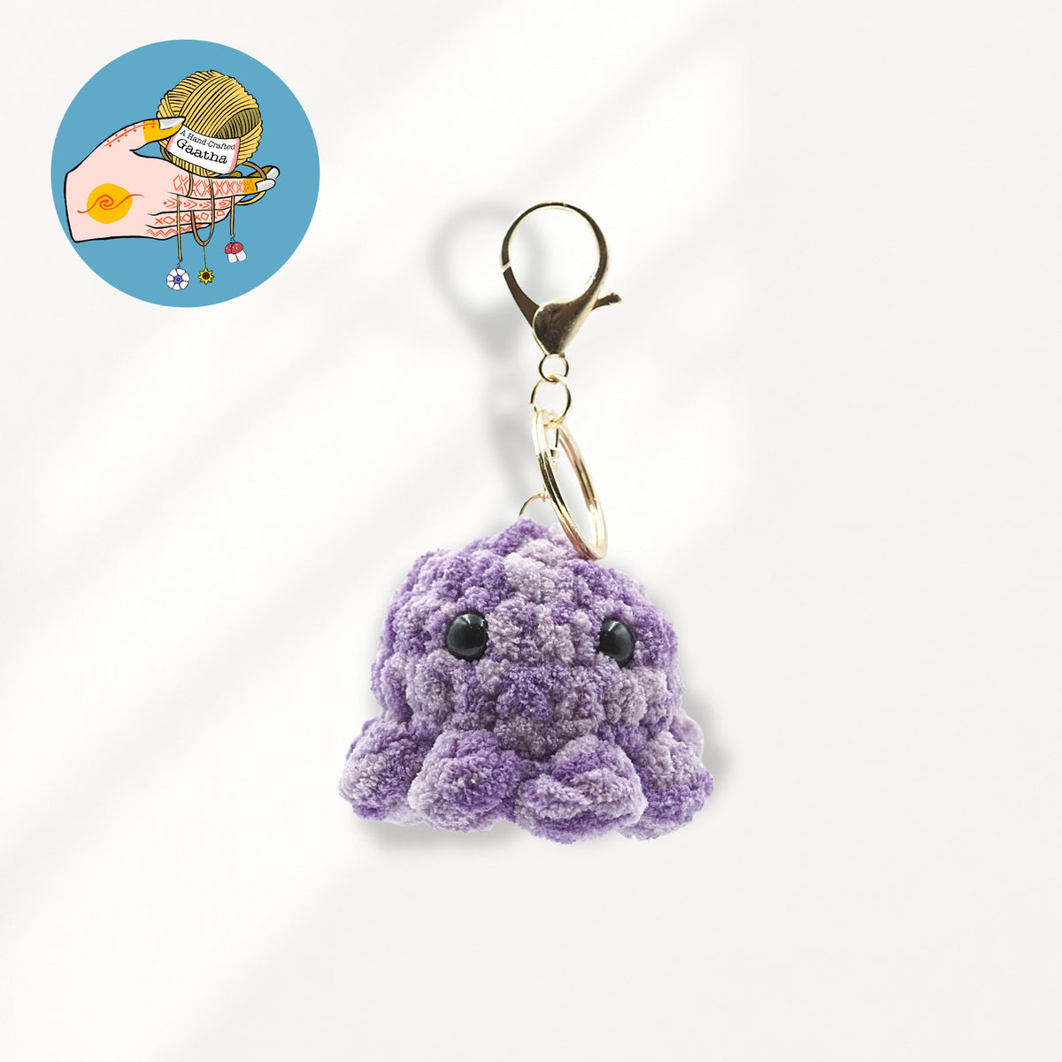 A small purple crocheted octopus keychain charm with black bead eyes and a gold-tone lobster clasp.
